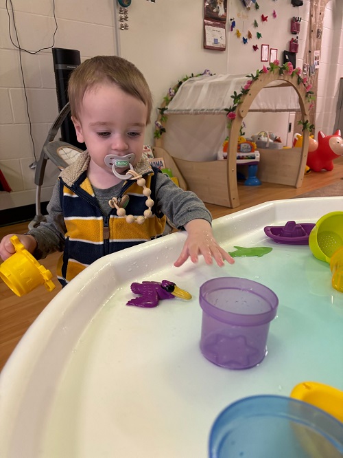 A child exploring the water in a tuff tray.