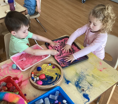 Two children engaging in sensory play at a table.