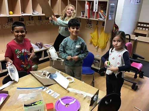group of children standing in front of their marble run creation made out of cardboard and tape and recyclables.