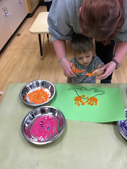 child with paint on their hands doing some hand painting to make a dinosaur