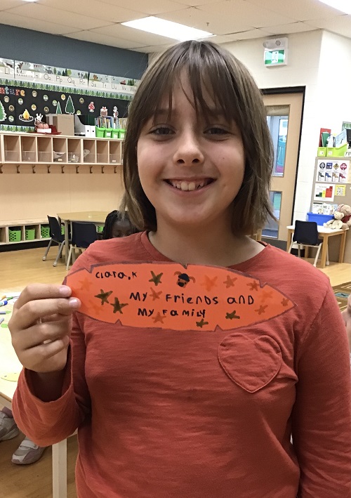child holding an orange paper feather with what she is thankful for written on it