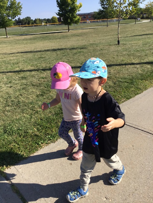 two children holding hands and walking along the sidewalk