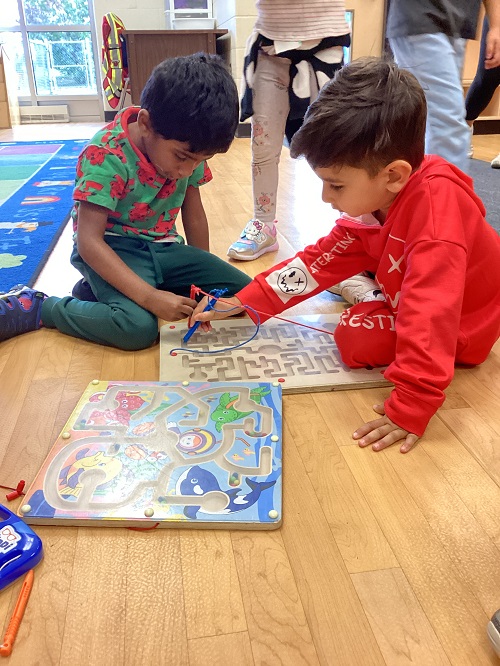 Two children sitting on the floor using a magneting maze board