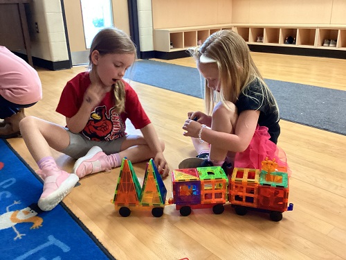 2 children sitting on the floor after they completed building a train out of magnatiles
