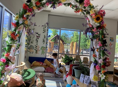 floral archway in classroom with greenery and pink orange and yellow flowers.