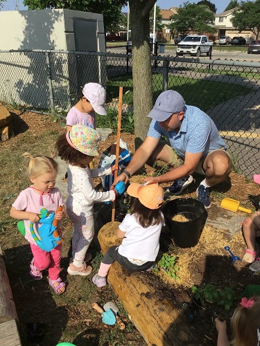 Parent helping plant garden with toddlers