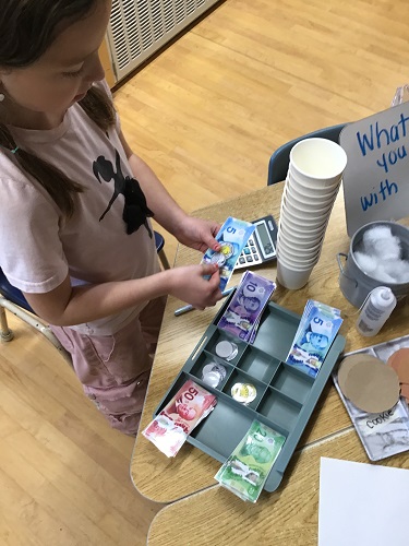 School Age child with fake money and a cash registered, some cups, and pretend coffee, she is counting the change