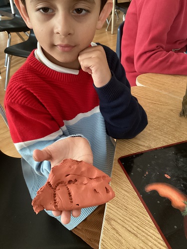 SK child holding a peice of clay in their hand with imprints on it