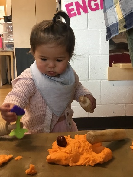 Infant exploring sensory play with orange playdough, cookie cutters and halloween decorations