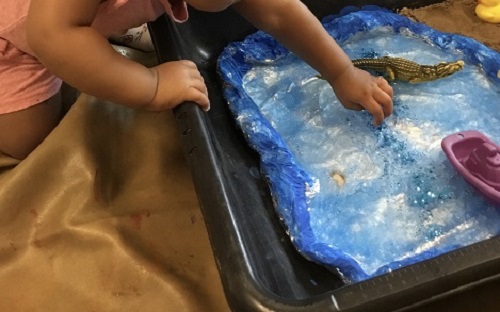 Infant child exploring sensory bin filled with gel and sea life animals