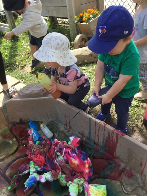 Two infant aged children squirting tie dye onto a sheet with squirt bottles