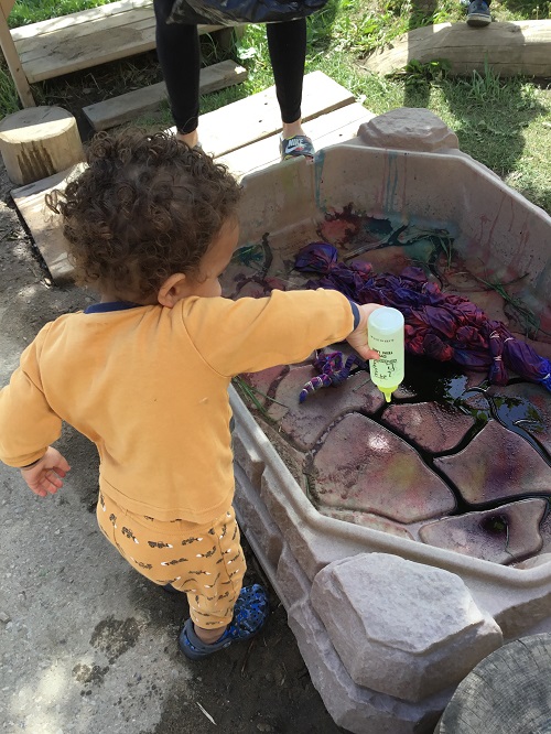 Infant aged child squirting tie dye onto a sheet in a plastic sensory bin