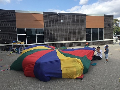 School age educator and children playing a parachute game