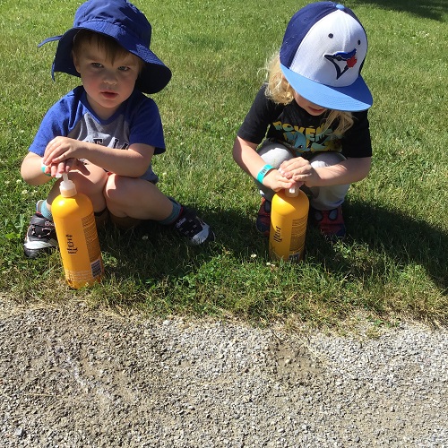 Two preschool boys enjoying water play at the park using shampoo bottles
