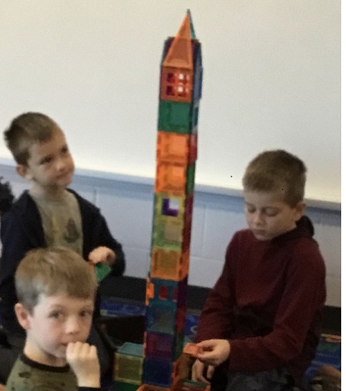 Three school age boys sittng on the floor around a magnetic tower they created