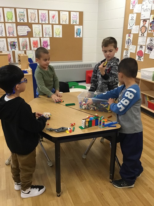 Four school age children surrounding a bucket of lego creating individual items