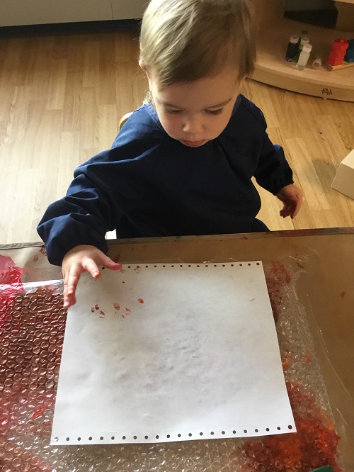 Toddler child pushing on white paper to transfer her bubble painting from bubble wrap