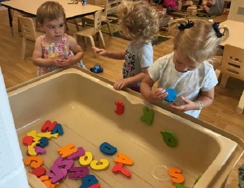 Three toddler children exploring a sensory bin filled with water and the alphabet