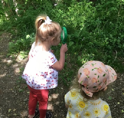 Toddler children using a magnifying glass in the forest 