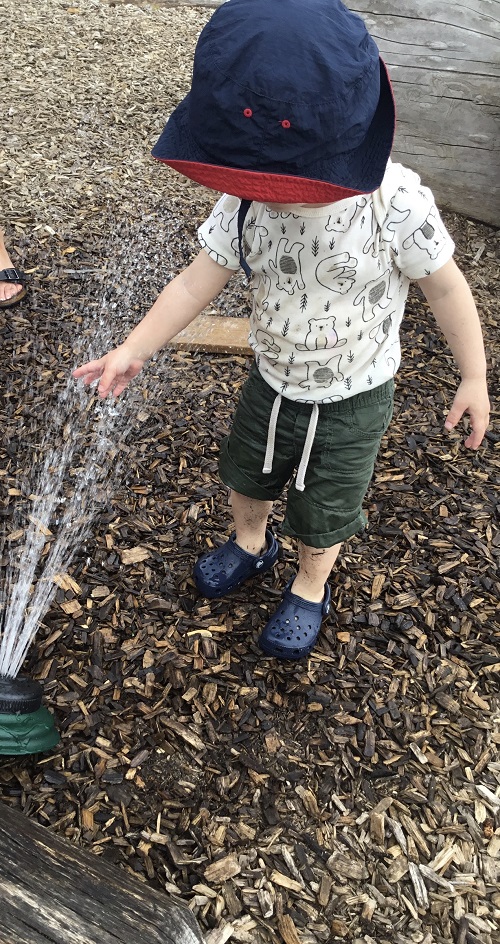Toddler boy playing in water sprinkler