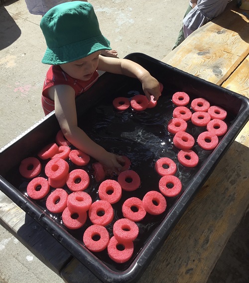Toddler aged boy playing in a sensory bin with donut pool noodles