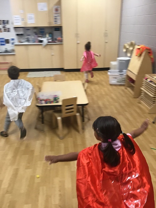 Preschool children running around a classroom pretending to be superheroes
