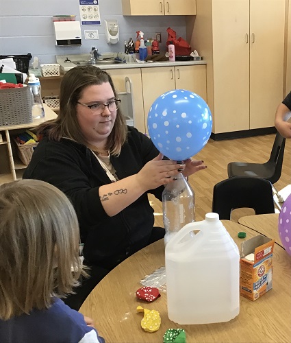 An educator holding a large balloon over a pop bottle