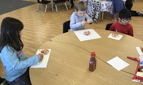 Children sitting at a table creating their own pizzas