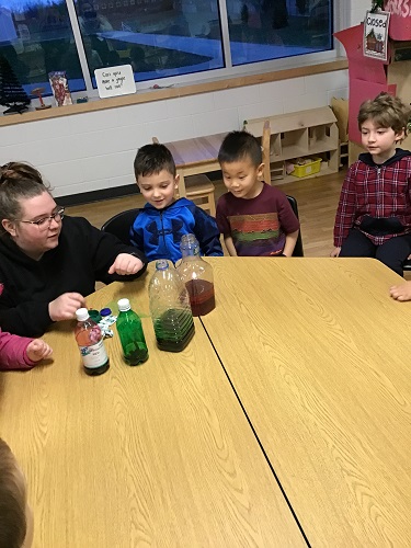 An educator and children sitting around a table looking at bottles filled with liquid