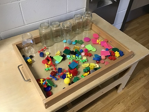A tray full of small, colourful loose parts and empty jars