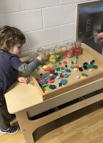 A child looking at the colourful loose parts on a tray and sorting them into jars