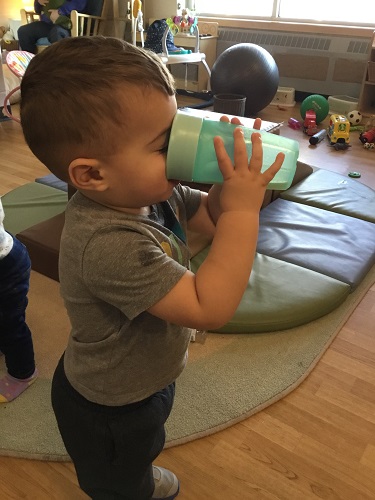 An infant drinking hand made apple juice out of a sippy cup