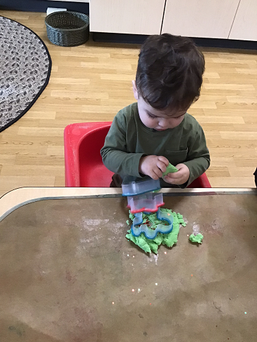 A child looking down at the playdough in his hands