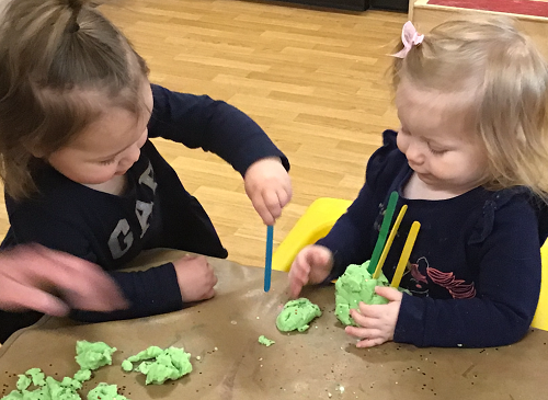Two children sticking popsicle sticks into the playdough in front of them