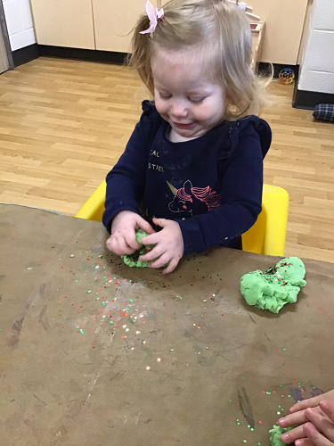 A child at a table squishing playdough in front of her