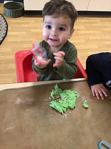 A child holding a cookie cutter with a pile of playdough in front of him 