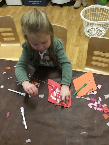 A child sitting at a table using glue and paper to create a kite