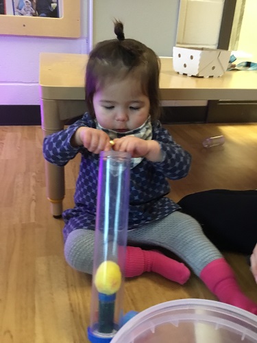 A child sitting on the floor putting items into a tube