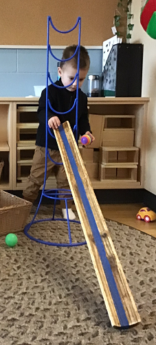 A child standing behind a ramp with a ball in his hand
