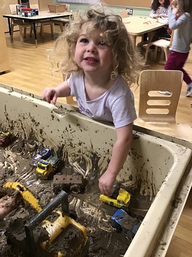 A child driving cars through mud in the sensory bin