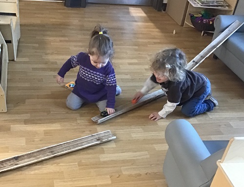 Two children using a long half tube as a ramp for their cars