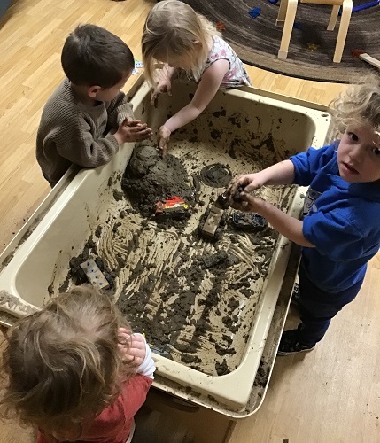 A group of children playing in a sensory bin filled with mud and vehicles