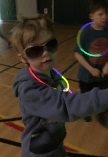 A boy wearing sunglasses and a glow necklace in the dark gym
