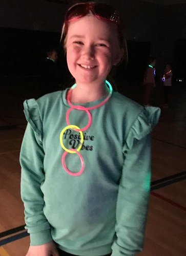 A child standing in a dark gym wearing a glow necklace