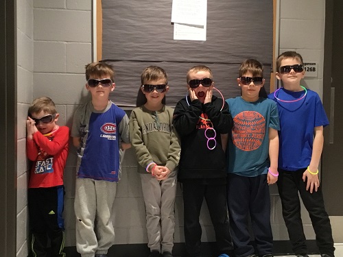 A group of children all wearing sunglasses standing against a wall