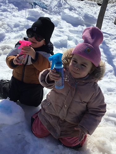 Two children sitting in the snow holding chalk paint spray bottles