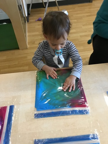 A child using his fingers to pushing down on a large ziploc bag filled with different colours of paint