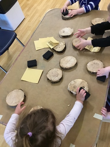 Children sitting around a table filled with wood cookies, sandpaper and foam paint brushes.