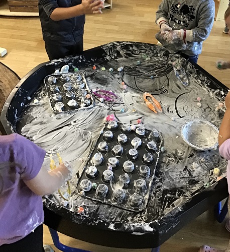 Children surrounding a tuff tray covered in shaving cream, cupcake trays and pompoms