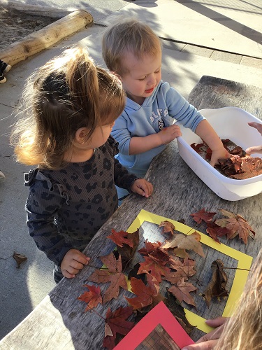 Two children playing with leaves at a table